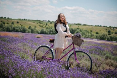 Genç bir kadın güneşli bir günde canlı lavanta tarlalarında bisiklet sürmekten zevk alıyor.