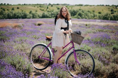 Genç bir kadın güneşli bir günde canlı lavanta tarlalarında bisiklet sürmekten zevk alıyor.