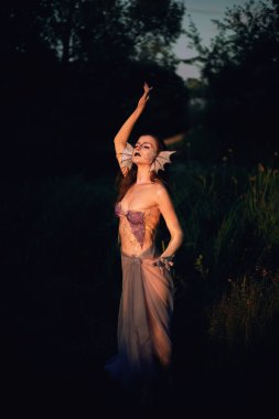 Deniz kızı akşam ışığında suyun yanında eşsiz özellikleri ve neşeli duruşuyla poz verir.