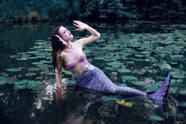 Huzurlu bir öğleden sonra etrafı nilüferlerle çevrili bir gölette uzanan denizkızı.