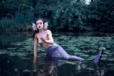 Huzurlu bir öğleden sonra etrafı nilüferlerle çevrili bir gölette uzanan denizkızı.