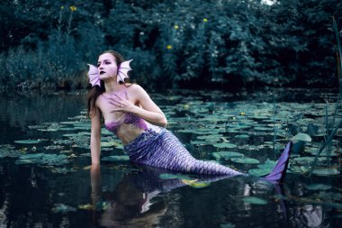 Huzurlu bir öğleden sonra etrafı nilüferlerle çevrili bir gölette uzanan denizkızı.