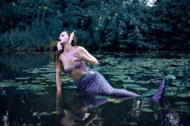 Huzurlu bir öğleden sonra etrafı nilüferlerle çevrili bir gölette uzanan denizkızı.