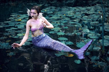 Huzurlu bir öğleden sonra etrafı nilüferlerle çevrili bir gölette uzanan denizkızı.