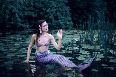 Huzurlu bir öğleden sonra etrafı nilüferlerle çevrili bir gölette uzanan denizkızı.