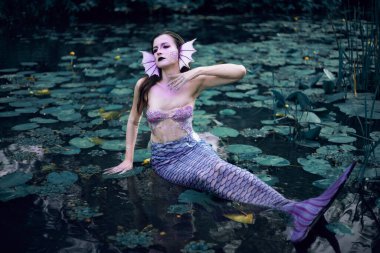 Huzurlu bir öğleden sonra etrafı nilüferlerle çevrili bir gölette uzanan denizkızı.