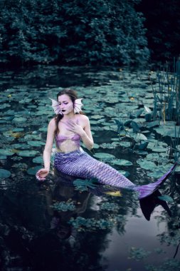 Huzurlu bir öğleden sonra etrafı nilüferlerle çevrili bir gölette uzanan denizkızı.