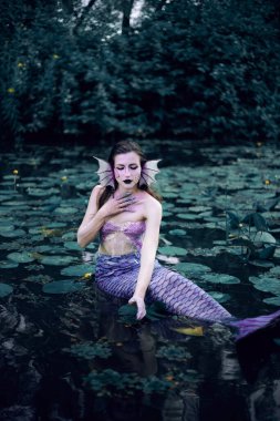 Huzurlu bir öğleden sonra etrafı nilüferlerle çevrili bir gölette uzanan denizkızı.