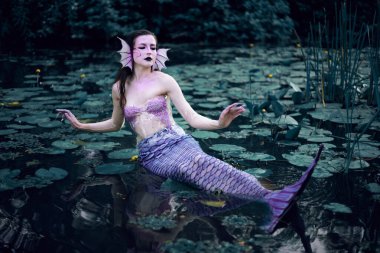 Huzurlu bir öğleden sonra etrafı nilüferlerle çevrili bir gölette uzanan denizkızı.