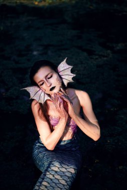 Deniz kızı, gün içinde bitkilerle çevrili, gizemli atmosferi olan doğal bir ortamda suyun yanında poz verir.