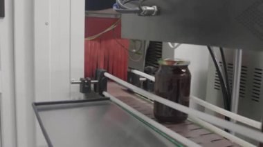 Altın bal dolu parlak cam kavanozlar fabrikadaki taşıyıcı bant boyunca hızla ilerler..