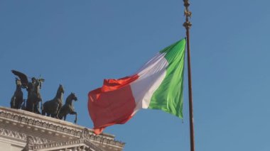ROME, ITALY - 1 Ağustos 2024: Canlı İtalyan bayrağı Roma görkemli mimarisinin üzerindeki renklerini göstererek nazikçe dalgalanıyor.