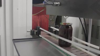 Altın bal dolu parlak cam kavanozlar fabrikadaki taşıyıcı bant boyunca hızla ilerler..