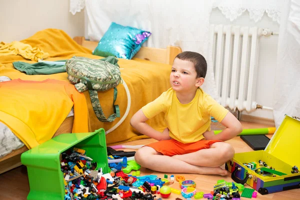 An unhappy child sits in a mess in his room