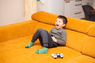 Evdeki turuncu kanepede otururken bilgisayar oyunu oynayan 5 yaşında tatlı bir çocuk..