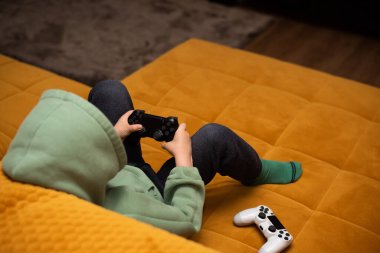 Evdeki turuncu kanepede otururken bilgisayar oyunu oynayan 5 yaşında tatlı bir çocuk..