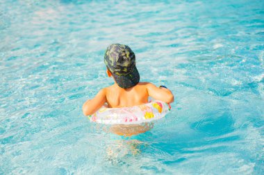 Mavi havuzda yüzen çocuk. Havuzda gülümseyen çocuk.