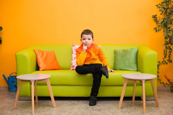 Lindo Niño Pensativo Suéter Naranja Brillante Sienta Sofá Verde — Foto de Stock