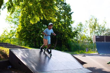 Yedi yaşında bir çocuk, korunmasız ve kasksız bir şekilde kaykayla yüksek bir tepeden kayıyor.