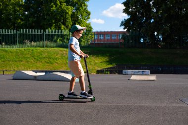 Yedi yaşında bir çocuk, kaykay parkında kaskı ve koruması olmadan scooter kullanıyor..
