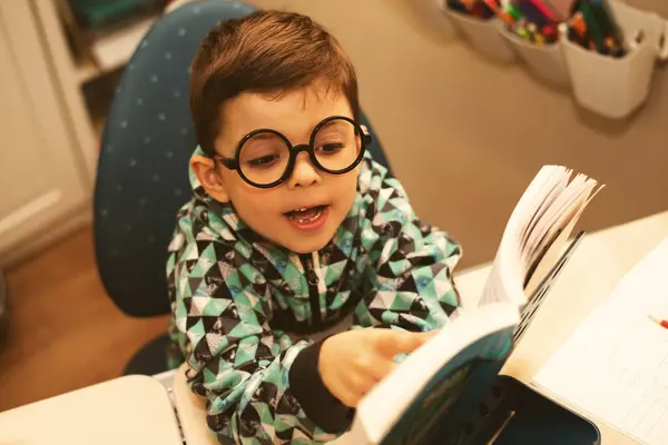 ラウンドメガネの小さな天才少年は 大きな興味を持つ厚い本を読みます — ストック写真