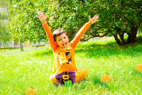 쾌활한 아이는 할로윈에 오렌지 의상에 잔디에 자신의 기뻐하고 가까운 사탕의 로열티 프리 스톡 사진