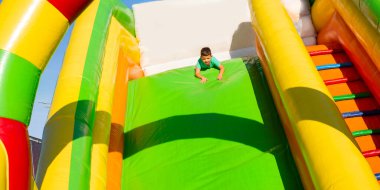 Küçük çocuk, şişme renkli bir kaydırağın üstünde baş aşağı gidiyor. Başı aşağı kayıyor