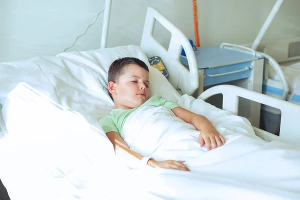 stock image A European seven-year-old boy in a light green T-shirt sleeps on a bed in a hospital room