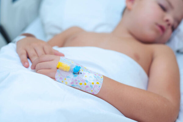Little 7-8 year old boy sleeps with a catheter in his hand in the hospital