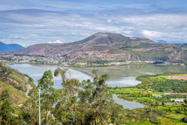 High view of the Yahuarcocha lake and surrounding trees and mountains, part of the Ecuadorian Andes, on a beautiful summer morning. Ibarra, Imbabura province, Ecuador.