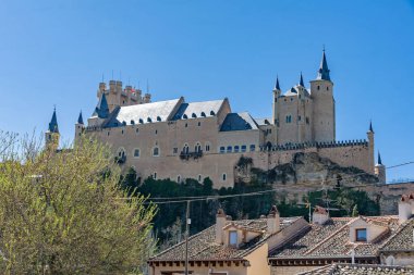 The Alczar of Segovia, Spain (c. 1120): This majestic royal fortress with distinctive slate spires stands on a rocky crag against a clear blue sky, a Spanish medieval landmark