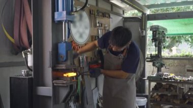Demirci makineyle sıcak metal çubuk çalıyor, 4K görüntü.