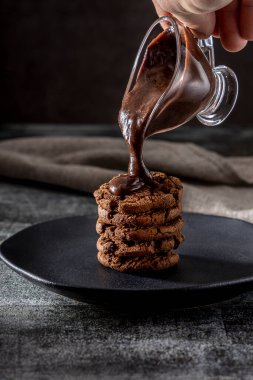 Çikolata parçacıklı kurabiye yığını. Dökülen erimiş çikolata sosu. 