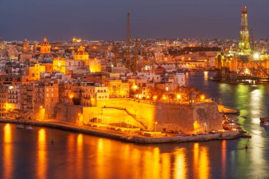 Malta, Valletta 'dan Grand Harbor boyunca uzanan tarihi Birgu (Vittariosa) kenti ve petrol platformu ve diğer sanayi tesislerinin gece panoramik görüntüsü