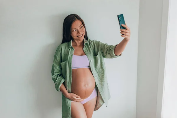 Hamile Bir Kadın Cep Telefonuyla Evde Çamaşırı Günlük Pamuk Gömlek — Stok fotoğraf