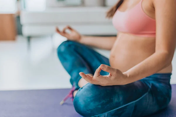 Prenatal yoga. Pregnant woman doing meditation. Woman meditating during Pregancy at home on floor mat in lotus position practicing breathing exercises. First and Second trimester training.