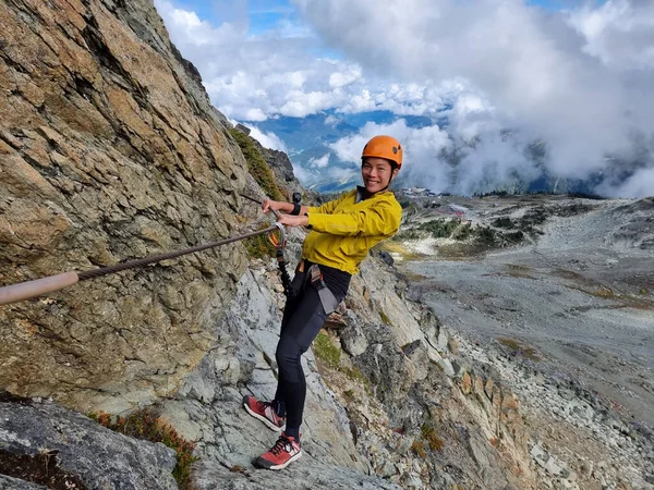 フェラタ登山ガイド付きツアーウィスラーピーク カナダの山側のハイパスでロープからぶら下がっている幸せなアジアの女性観光客旅行 — ストック写真