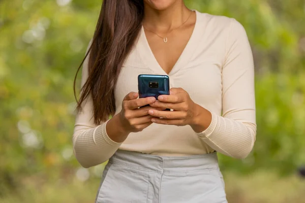 Woman holding phone using hands texting app while walking in forest. Closeup of cellphone and midsection. Sustainability, nature lifestyle people connected online.