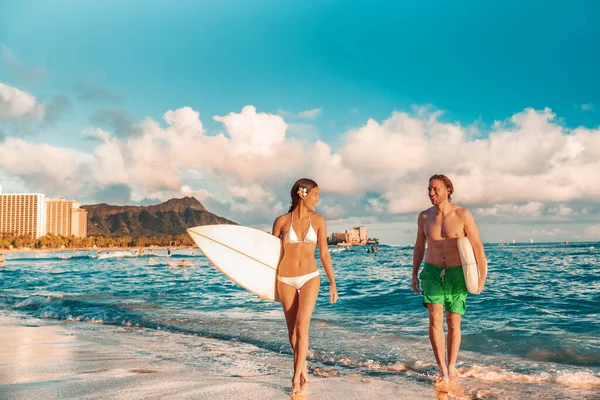 Hawaii Honolulu couple surfers happy on waikiki beach with surfboards. Healthy active sport lifestyle fitness people at sunset with diamond head mountain landscape.