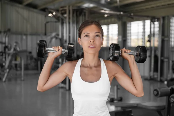 Gym workout fit woman lifting dumbbell weights doing shoulder press in fitness center. Healthy active people training of Asian woman holding free weight.