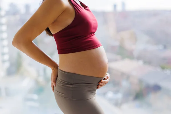 Pregnant woman with lower back pain due to sciatica tired. Health during pregnancy. Close up of belly in profile if expectant mother in yoga sports fitness outfit.