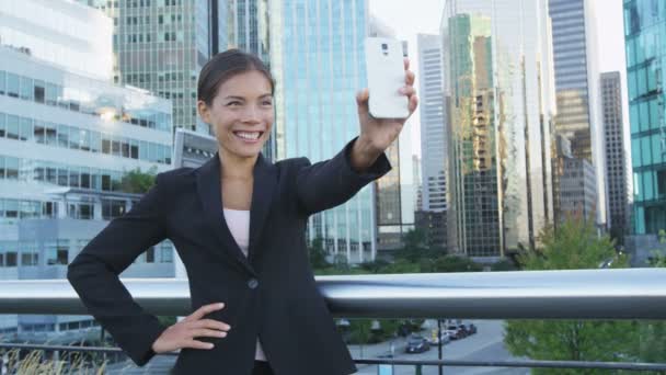商界女性在社交媒体上使用智能手机应用程序自拍自拍照 年轻的女商人在户外穿着西装夹克 用智能手机开心地笑着 城市女性专业人员 — 图库视频影像