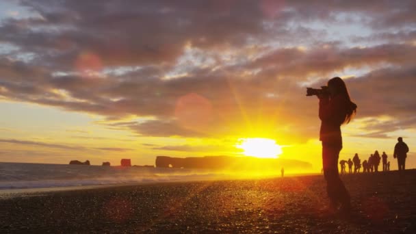 アイスランドの写真家が日没時に一眼レフカメラを使って写真を撮る観光客アイスランド南海岸のヴィク レイニサフィアラ黒砂のビーチを歩いています 観光地を訪れる女性 レッド エピック スローMo — ストック動画