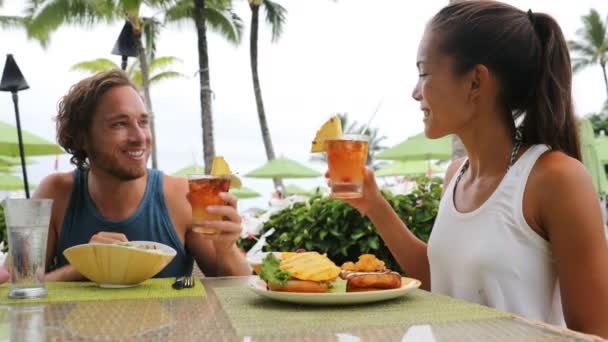 情侣约会有酒类饮料迈泰鸡尾酒在夏威夷的海滩俱乐部饮酒的乐趣 浪漫的年轻混血种族画像夫妇在蜜月浪漫之旅在夏威夷的海滩上 — 图库视频影像