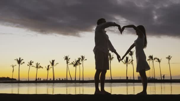 浪漫的夫妻在日落时形成了心形 他们的臂膀是爱情的象征 就像夕阳西下的大海 恋爱中的女人和男人一起庆祝蜜月 红色Epic慢速运动 — 图库视频影像