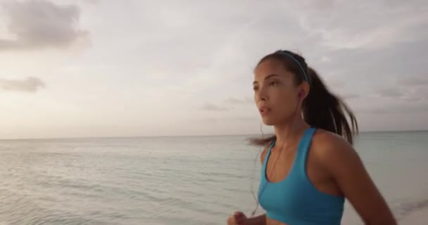 ランニングモチベーション 夏のビーチの背景にイヤフォンを身に着けているスポーツブラジャーやネオンショートパンツの服で音楽ジョギングとランナーのトレーニング — ストック動画