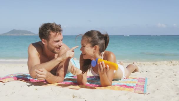 海滨夫妇一边笑一边晒日光浴 把防晒霜涂在脸上 并在假日放松一下 成年人 女人和男人躺在美丽的海滩上的白沙滩上 — 图库视频影像