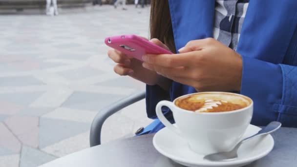 屋外テラスカフェでアプリ飲料コーヒーを使用して スマートフォンで都市部の専門家のビジネス女性のテキストメッセージやニュースを読む レストランやカフェのヨーロッパ市内中心部の通り — ストック動画
