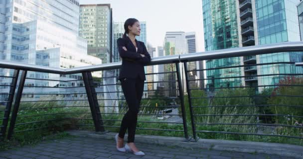 身穿黑色西服的年轻亚洲女商人站在城景阳台上 双臂交叉 若有所思地望向远方的低角度全景 复制空间 — 图库视频影像