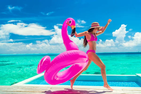 面白いインフレータブルピンクフラミンゴプールでビキニで休暇楽しい女性は無限のスイミングプールでジャンプ喜びの実行を浮かべています リゾートで旅行の休日を楽しむ女の子豪華な水上バンガロー旅行 — ストック写真